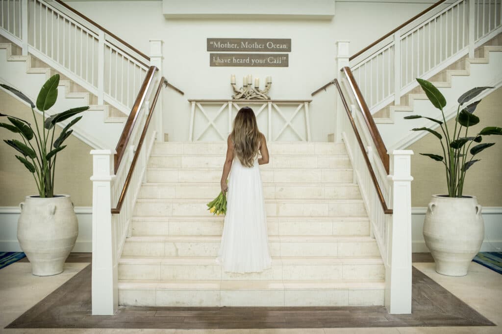 bride walking up white staircase holding small bouquet of green and white flowers at margaritaville resort orlando wedding venue